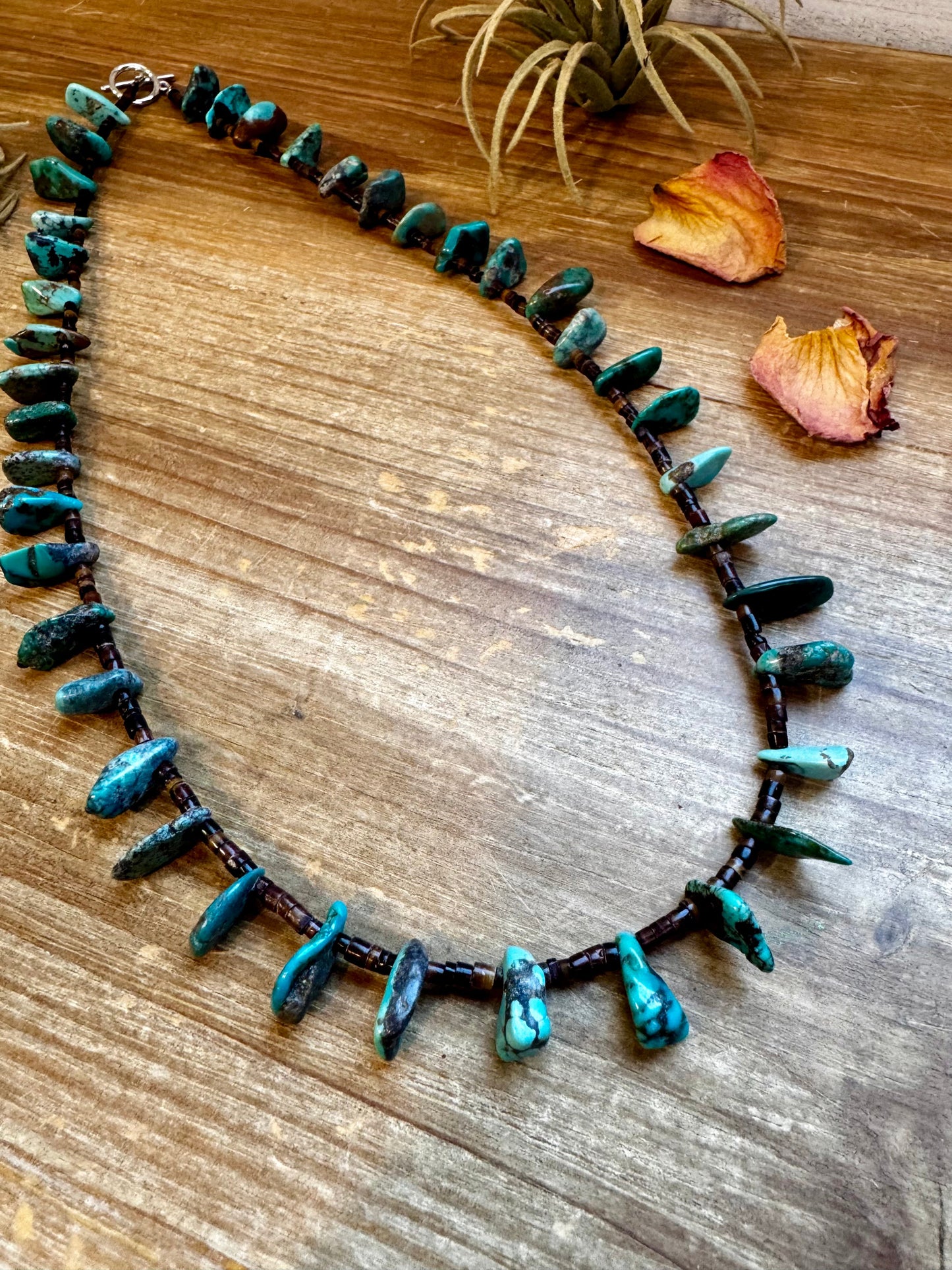Close-up of a 4-inch long handmade earring with 3-inch extender, featuring 3mm dark shell beads and a real turquoise teardrop pendant. Silver-plated finish. Each turquoise stone is unique. Made in the USA by The Bijoux FAB.