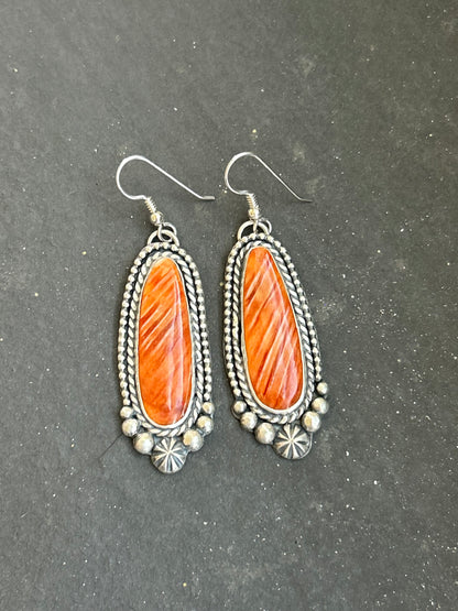 These handcrafted sterling silver dangle earrings by artist Shay Pfeiffer feature beautiful orange spiny oyster stones that glow with rich, warm tones. Each stone is hand-selected and set in sterling silver, showing off the natural variations that make every pair unique. Lightweight with just the right amount of movement, these earrings add a bold yet refined touch to any outfit.
Made in the USA and purchased directly from Shay Pfeiffer, these are wearable works of art.
Sterling silver dangle earrings
Orang