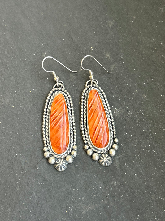 These handcrafted sterling silver dangle earrings by artist Shay Pfeiffer feature beautiful orange spiny oyster stones that glow with rich, warm tones. Each stone is hand-selected and set in sterling silver, showing off the natural variations that make every pair unique. Lightweight with just the right amount of movement, these earrings add a bold yet refined touch to any outfit.
Made in the USA and purchased directly from Shay Pfeiffer, these are wearable works of art.
Sterling silver dangle earrings
Orang